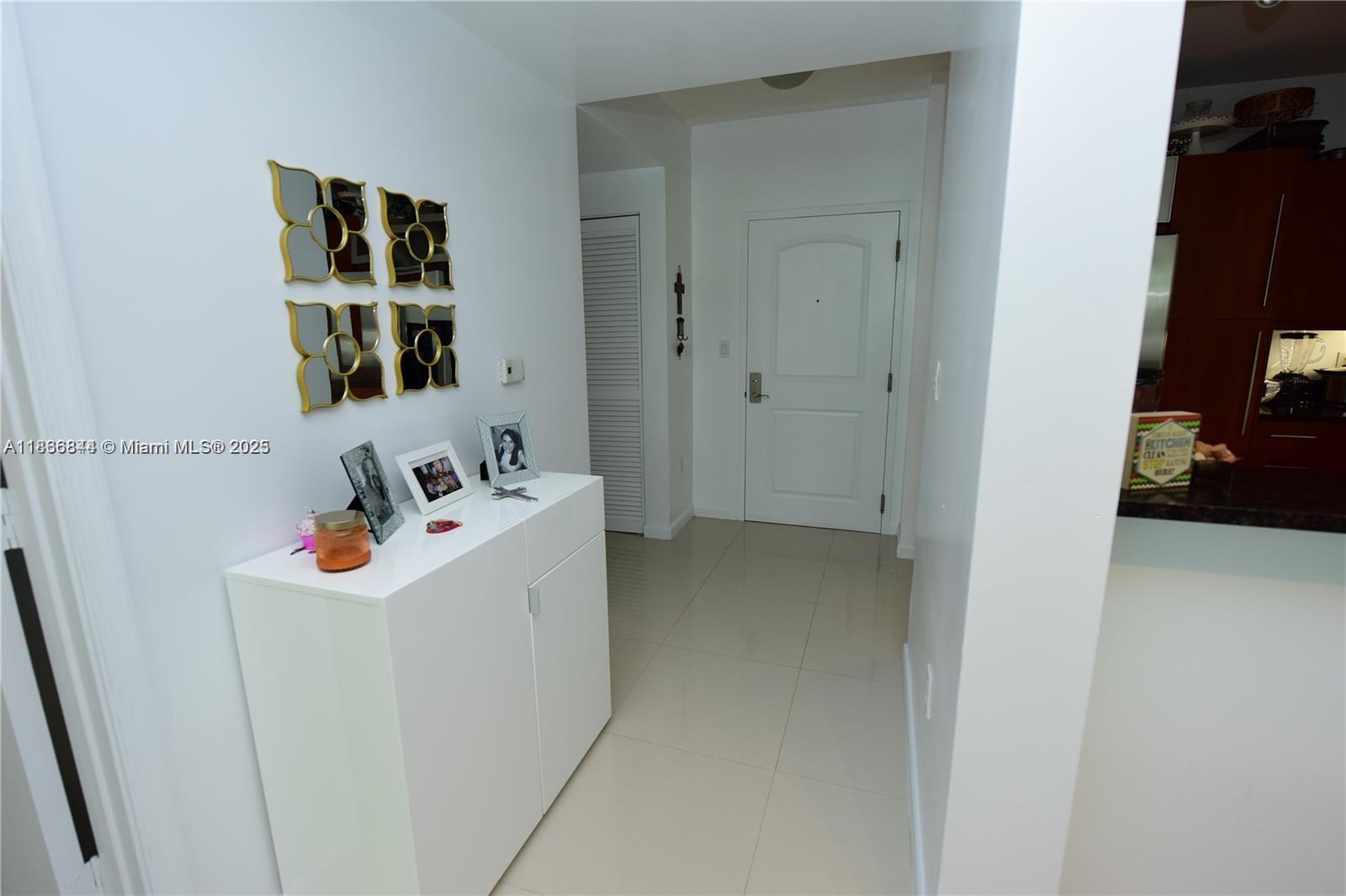 A white entryway features a console table, wall decor, and tile flooring leading to a door — 7355 SW 89th St # 622N, Miami FL 33156, MIAMI, FL