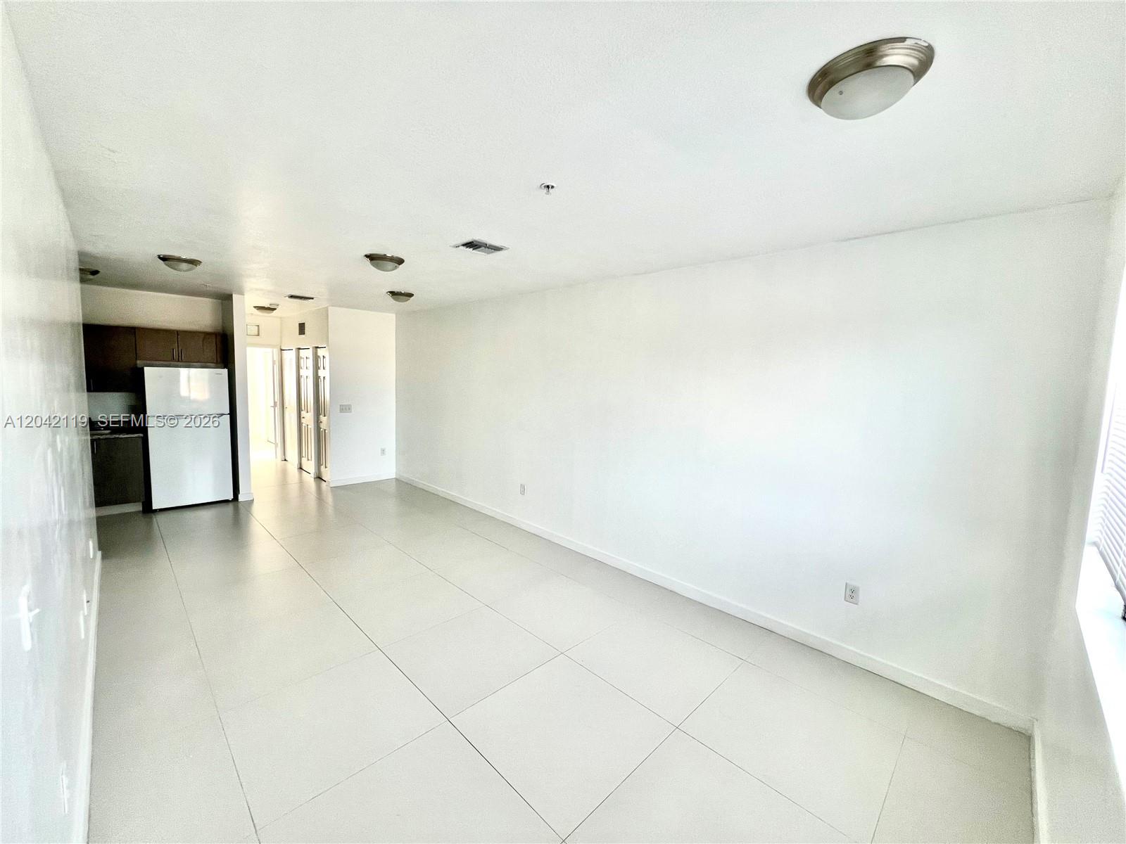 A bright, open-concept living area features white walls, large light-colored floor tiles, and a kitchen — 440 E 27th St # 204, Hialeah FL 33013, HIALEAH, FL