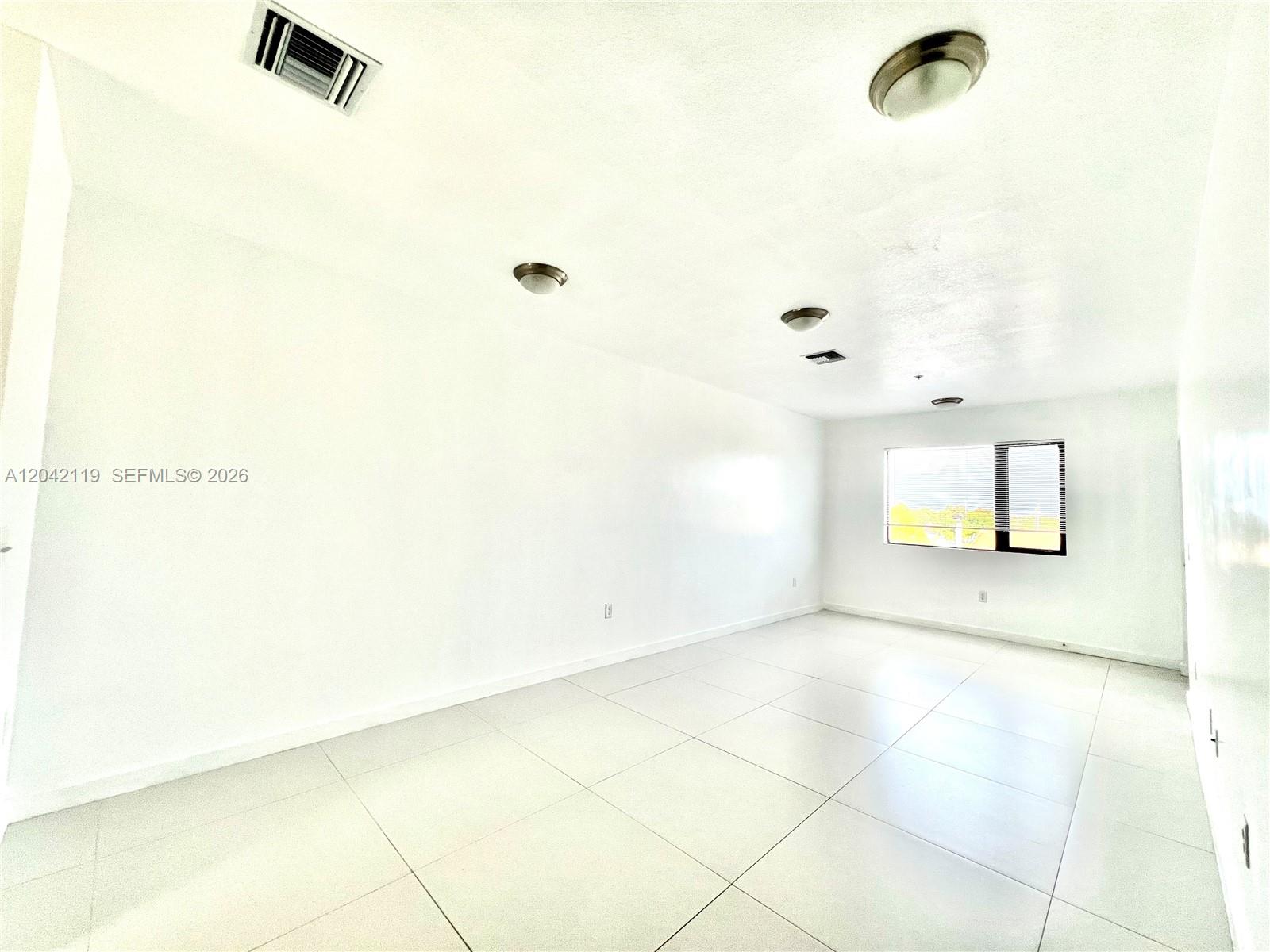 An empty room features white walls, large light-colored floor tiles, and a single window — 440 E 27th St # 204, Hialeah FL 33013, HIALEAH, FL