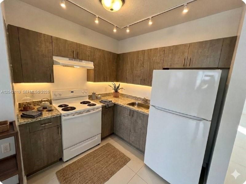 A kitchen features wood-grain cabinets, a white stove, a white refrigerator, and track lighting — 440 E 27th St # 204, Hialeah FL 33013, HIALEAH, FL
