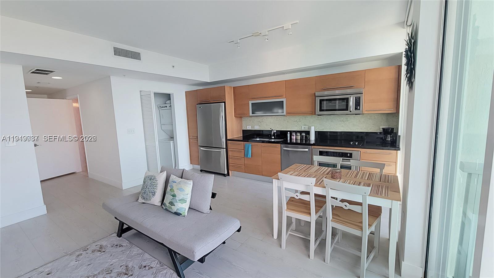 A modern kitchen with light wood cabinets and stainless steel appliances sits beside a dining area — 253 NE 2nd St # 3305, Miami FL 33132, MIAMI, FL