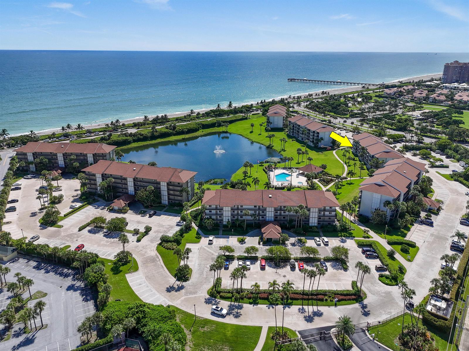 An aerial view shows a multi-building apartment complex with a central pond and pool — 501 S Seas Drive # 206, Jupiter FL 33477, JUPITER, FL