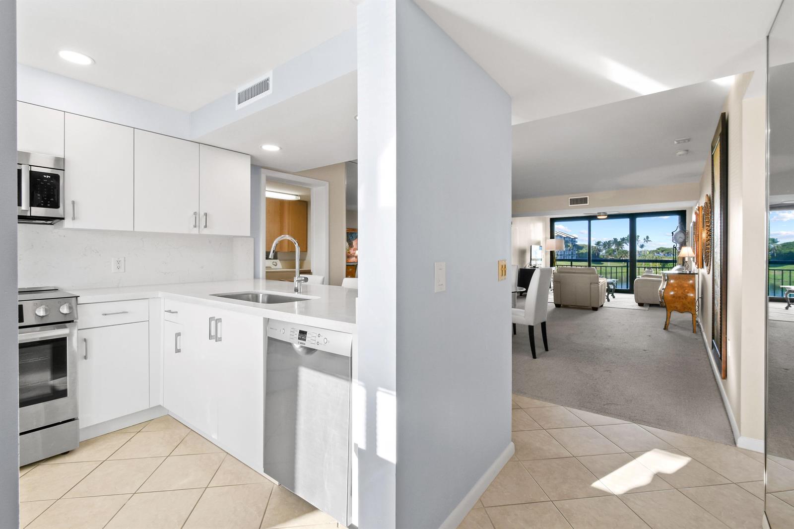 A white kitchen with stainless steel appliances opens into a carpeted living area with balcony views — 501 S Seas Drive # 206, Jupiter FL 33477, JUPITER, FL