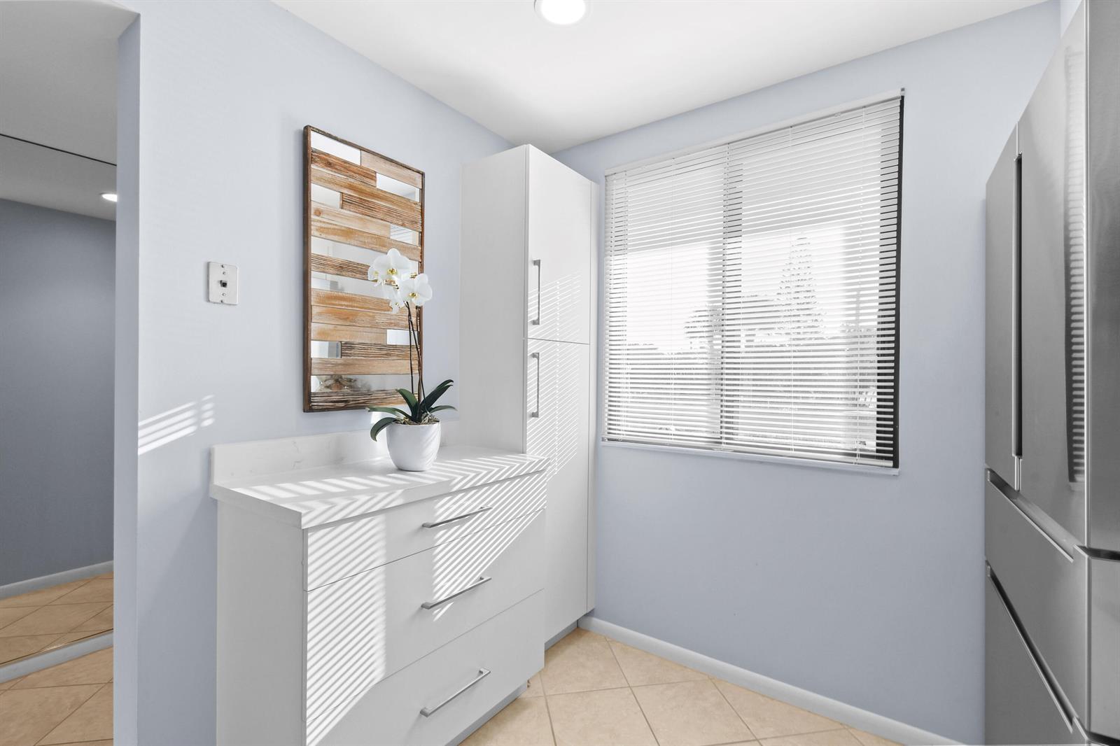 A kitchen area features white cabinetry, a countertop, a potted orchid, and a window with blinds — 501 S Seas Drive # 206, Jupiter FL 33477, JUPITER, FL