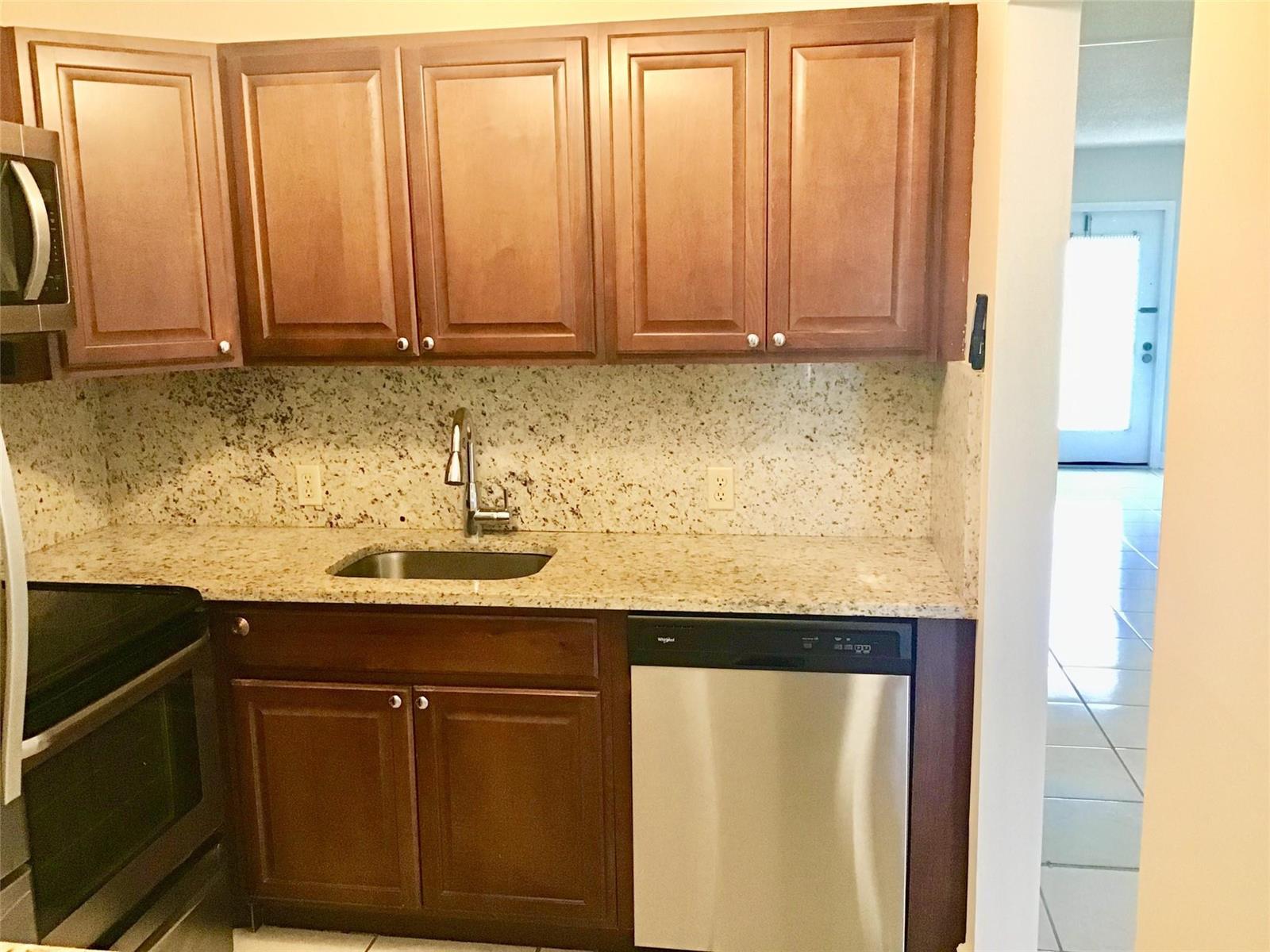A kitchen features dark wood cabinets, granite countertops, a stainless steel dishwasher, and a sink — 135 Fanshaw D # 135, Boca Raton FL 33434, BOCA RATON, FL