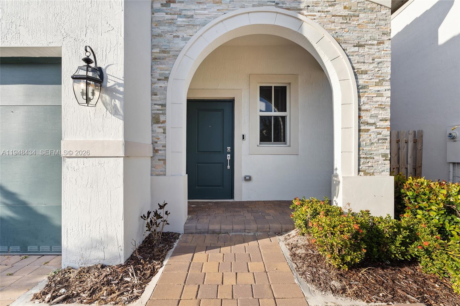 A paved walkway leads to a dark green front door under a stone-accented arched entryway — 2405 NW 131st Cir, Miami FL 33167, MIAMI, FL