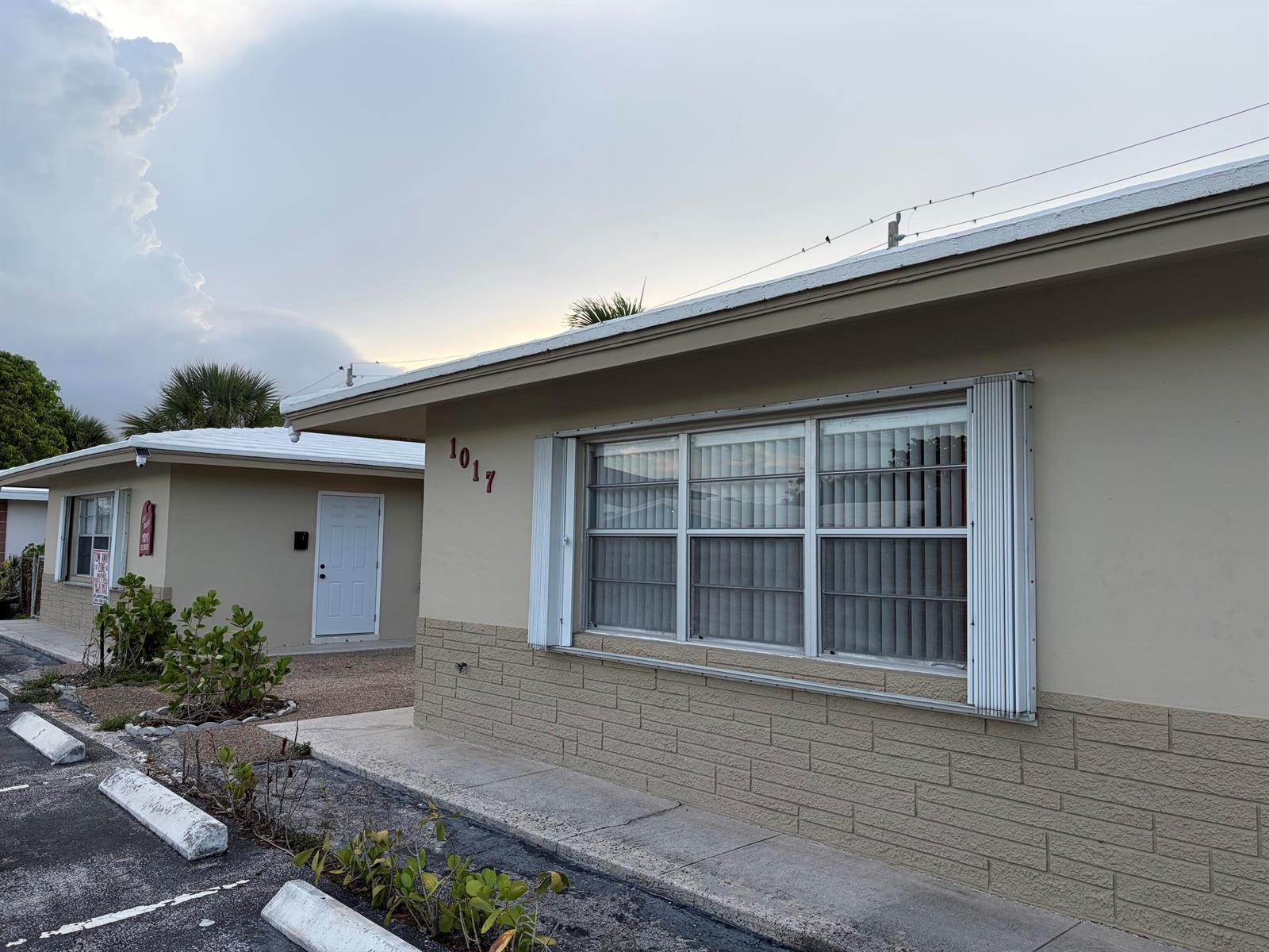 Exterior view of a single-story building with tan stucco walls, brick siding, and a large window — 1017 SE 3rd Street # 4, Deerfield Beach FL 33441, DEERFIELD BEACH, FL