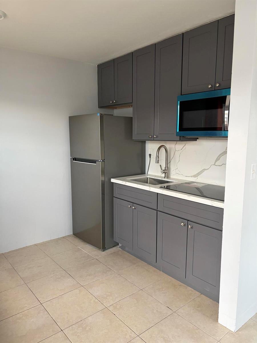 A small kitchen features gray cabinets, stainless steel appliances, and a white marble-patterned backsplash — 1017 SE 3rd Street # 4, Deerfield Beach FL 33441, DEERFIELD BEACH, FL