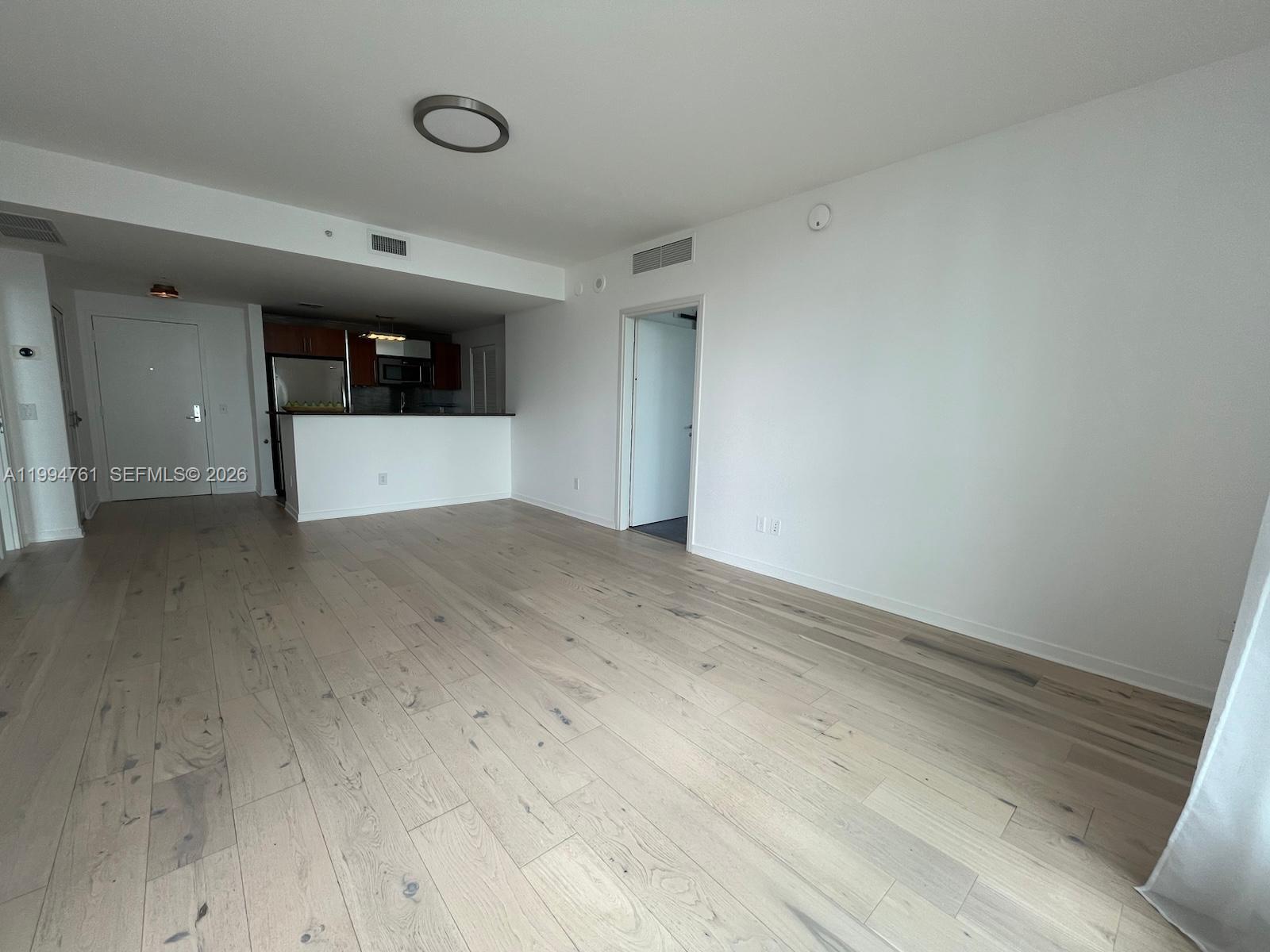 An open-concept living area features light wood flooring, white walls, and a kitchen island — 300 S Biscayne Blvd # 2012, Miami FL 33131, MIAMI, FL