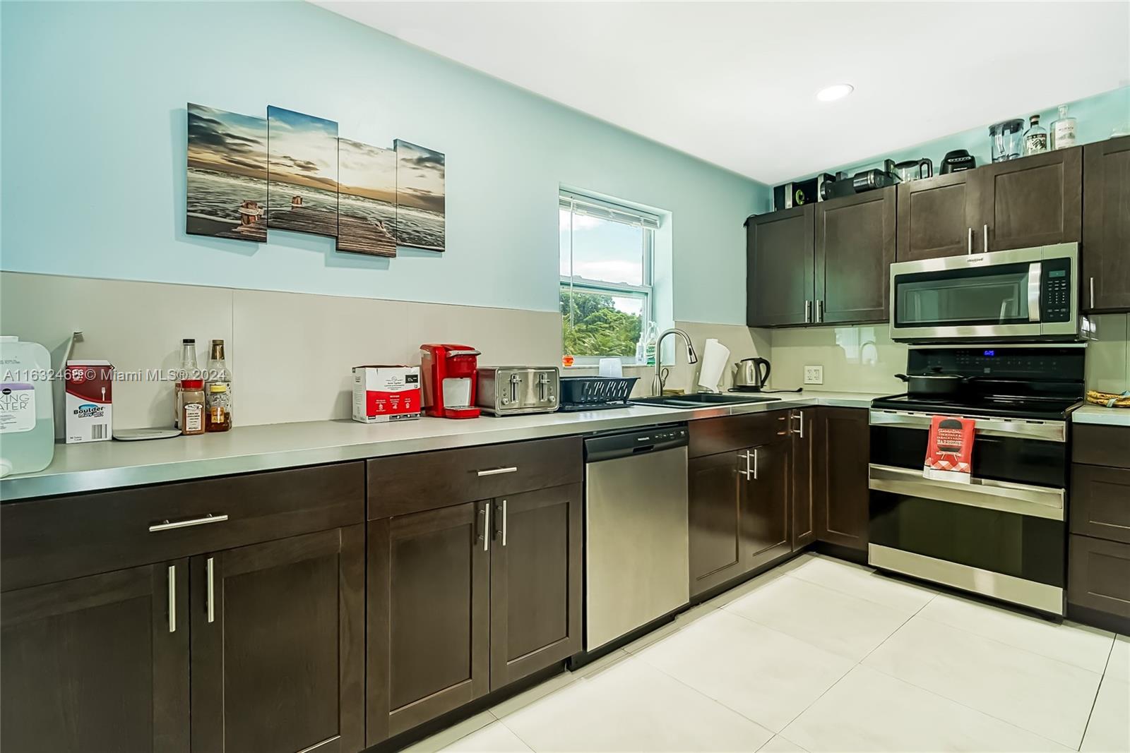 A kitchen features dark wood cabinets, stainless steel appliances, and light blue walls — 216 SW 6th St, Hallandale Beach FL 33009, HALLANDALE BEACH, FL