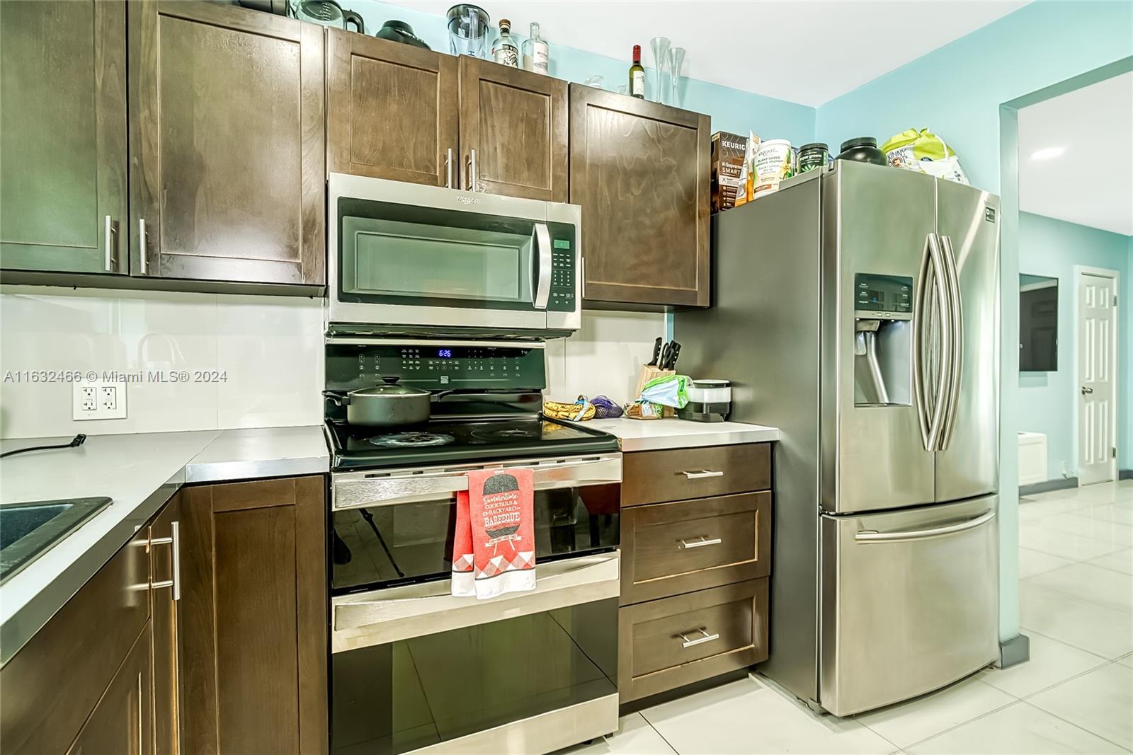 A kitchen features dark wood cabinets, stainless steel appliances, and a light blue wall — 216 SW 6th St, Hallandale Beach FL 33009, HALLANDALE BEACH, FL