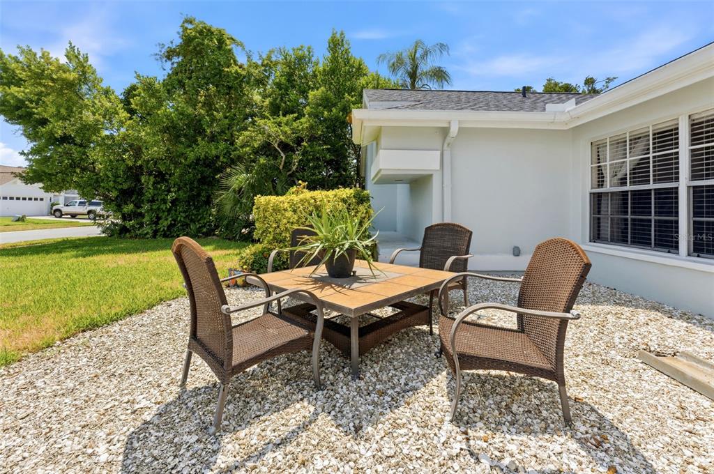 A patio with a square table and four wicker chairs sits on a gravel surface — 1763 PEBBLE HILL COURT, PALM HARBOR, FL