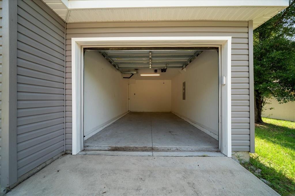 An empty one-car garage with gray vinyl siding, a concrete floor, and a white interior — 37 WATER TRACK COURSE, OCALA, FL