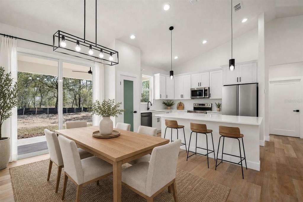 A modern kitchen and dining area with white cabinetry, a center island, and wood flooring — 1133 W NANKEEN DRIVE, DUNNELLON, FL