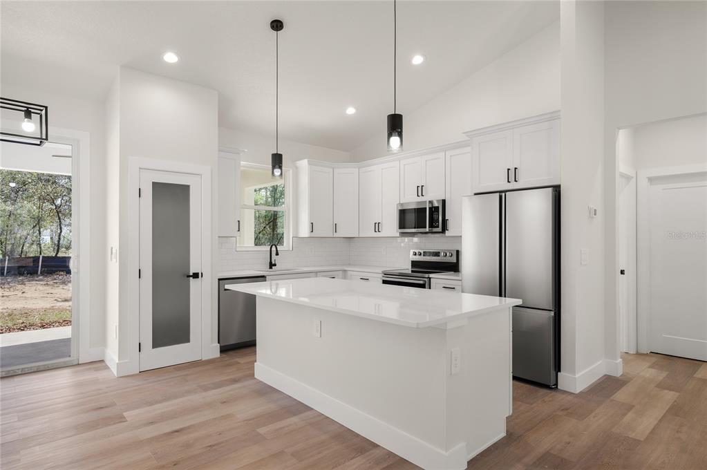 A modern kitchen features white cabinets, a central island, stainless steel appliances, and wood flooring — 1133 W NANKEEN DRIVE, DUNNELLON, FL