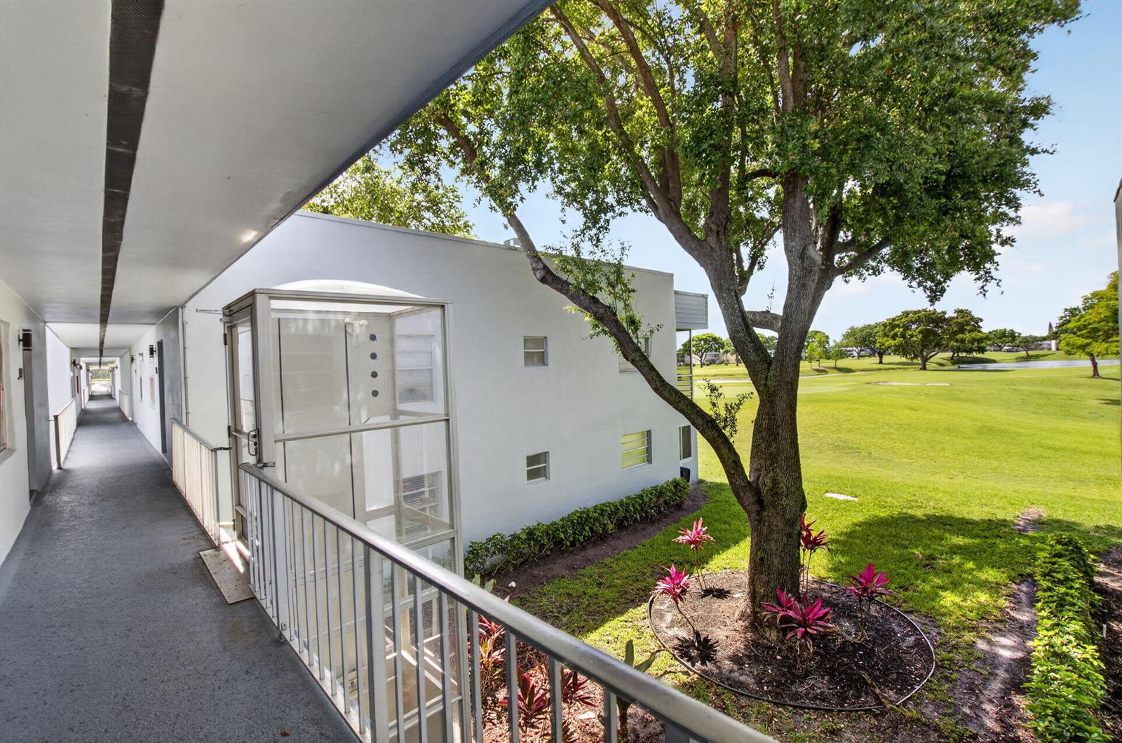 An exterior view of an apartment building balcony featuring a glass elevator and golf course view — 955 Normandy Trail, Delray Beach FL 33484, DELRAY BEACH, FL