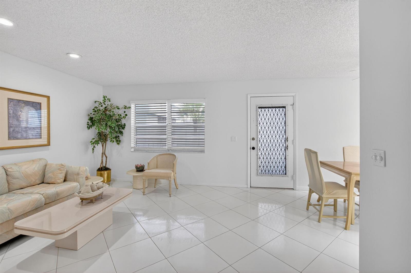 A bright living and dining area features white tile floors, a sofa, and a front door — 955 Normandy Trail, Delray Beach FL 33484, DELRAY BEACH, FL