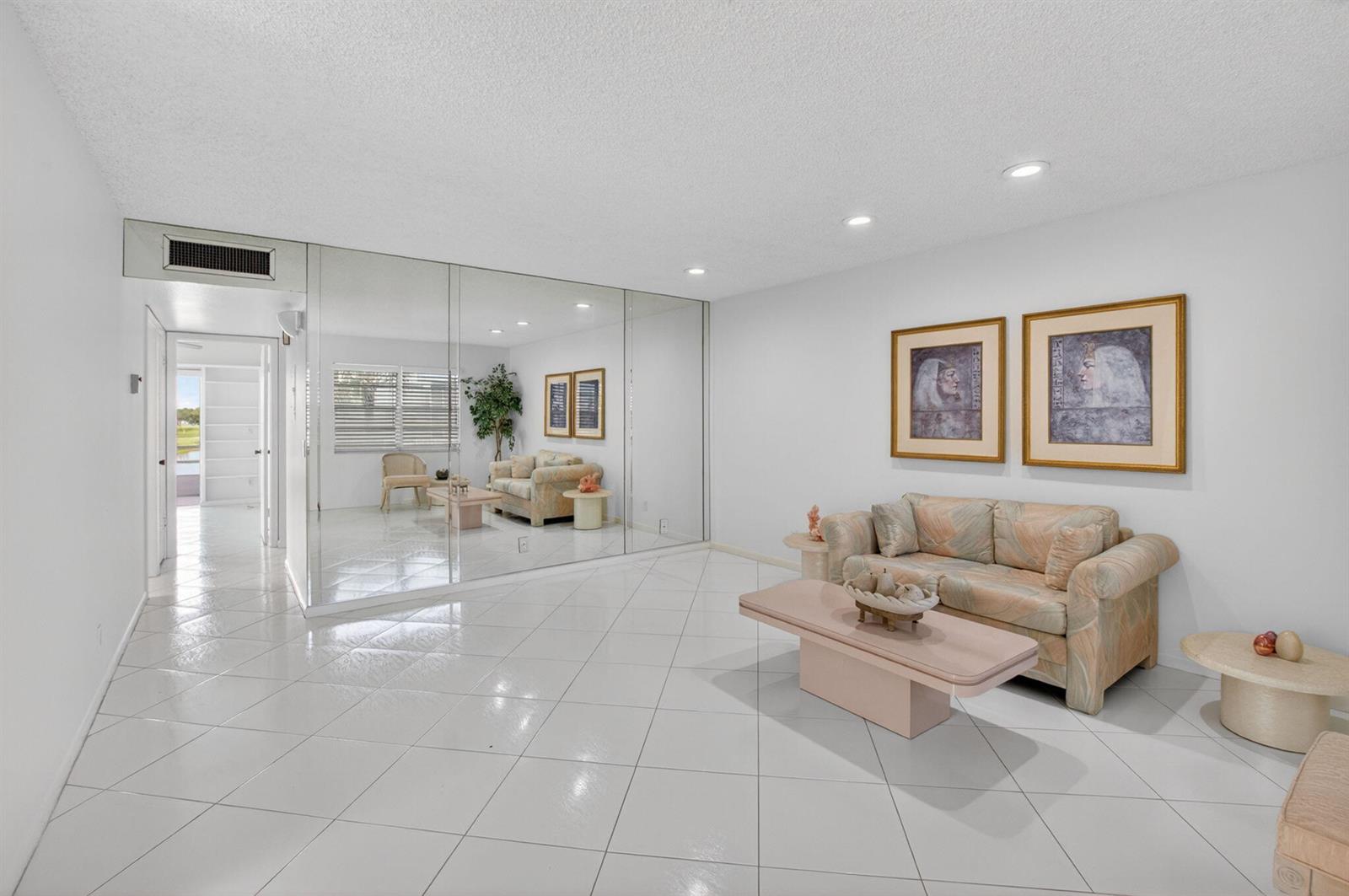 A living room with white tile floors, a mirrored wall, and a patterned sofa — 955 Normandy Trail, Delray Beach FL 33484, DELRAY BEACH, FL