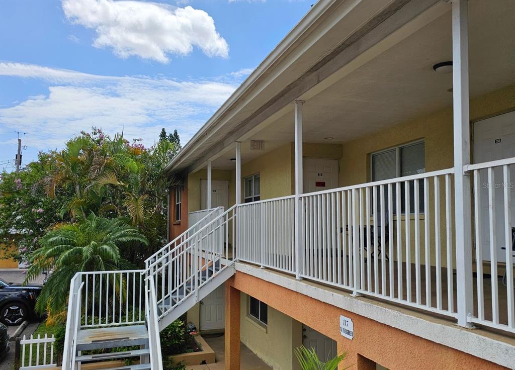 An exterior view of a two-story apartment building with a white metal staircase and railing — 117 N EVERGREEN AVENUE UNIT 201, CLEARWATER, FL
