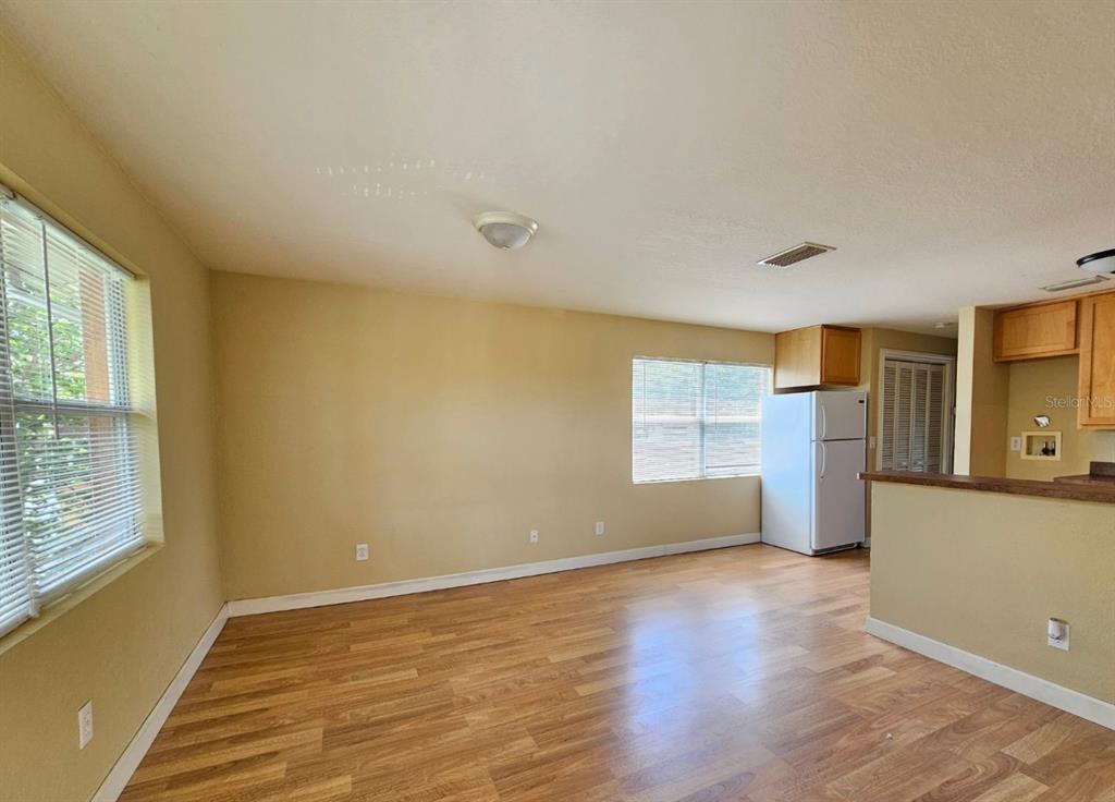 An empty room with light-colored walls, wood-look flooring, a window, and an adjacent kitchen area — 117 N EVERGREEN AVENUE UNIT 201, CLEARWATER, FL