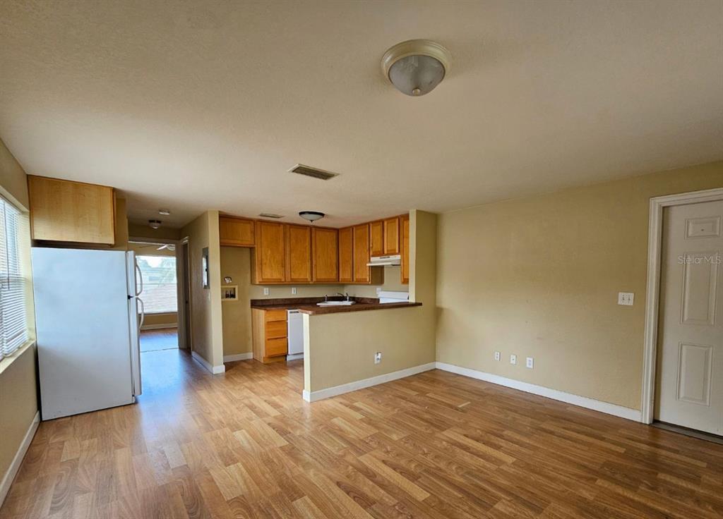 An open-concept kitchen with wood cabinets and a breakfast bar overlooks a living area — 117 N EVERGREEN AVENUE UNIT 201, CLEARWATER, FL