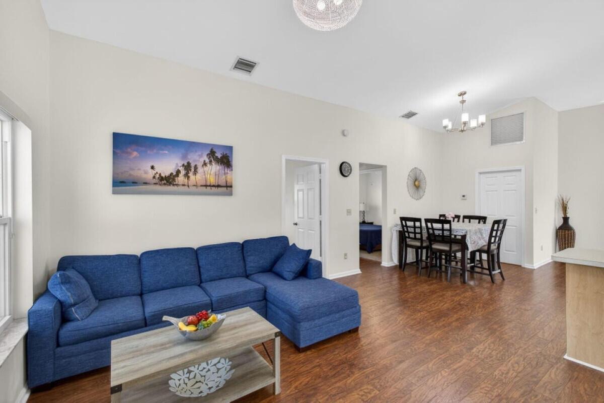 A living room with a blue sectional sofa, wood-look flooring, and an adjacent dining area — 6223 Kendrick Street, Jupiter FL 33458, JUPITER, FL