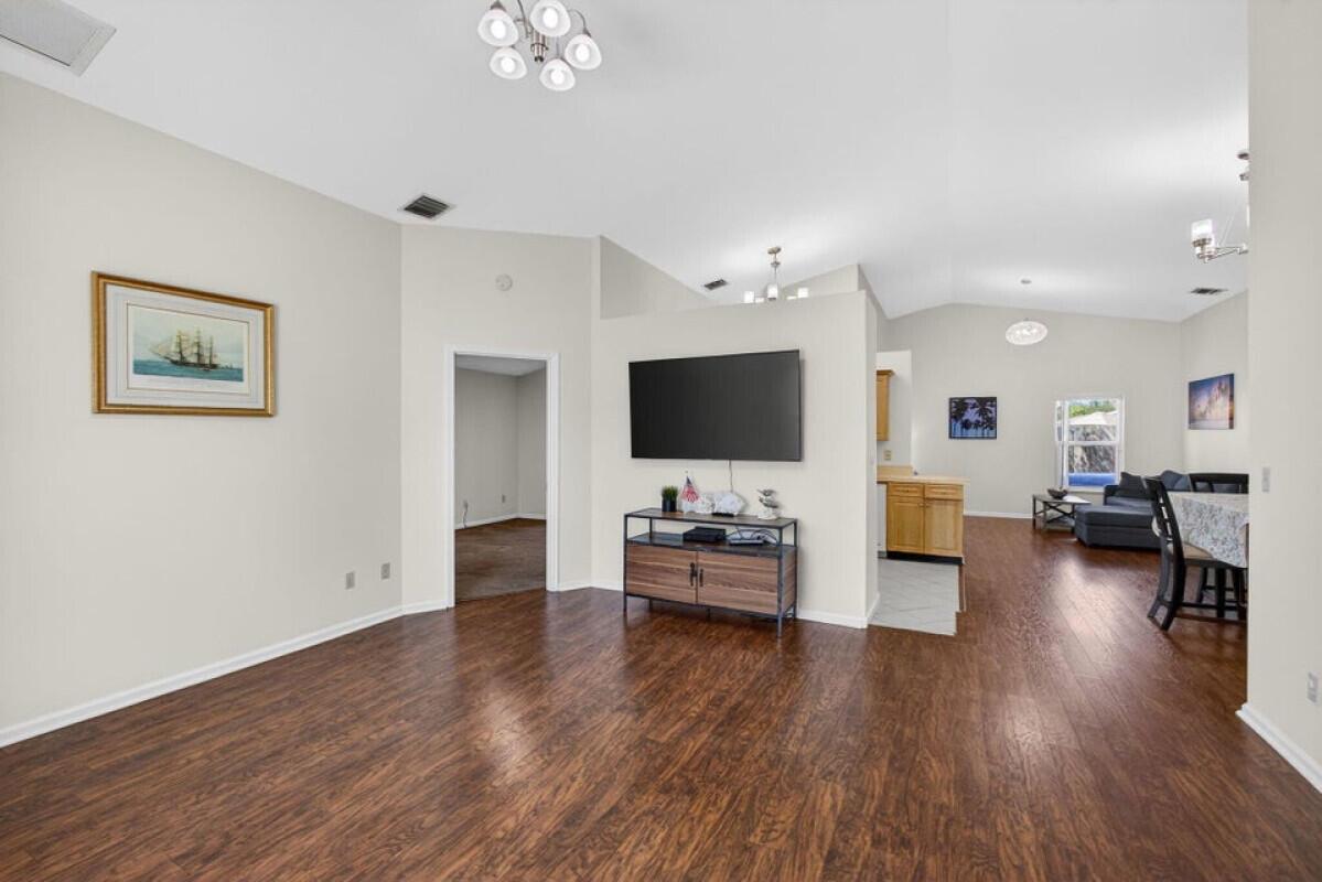 A living room with wood-look flooring, a wall-mounted television, and an open kitchen area — 6223 Kendrick Street, Jupiter FL 33458, JUPITER, FL