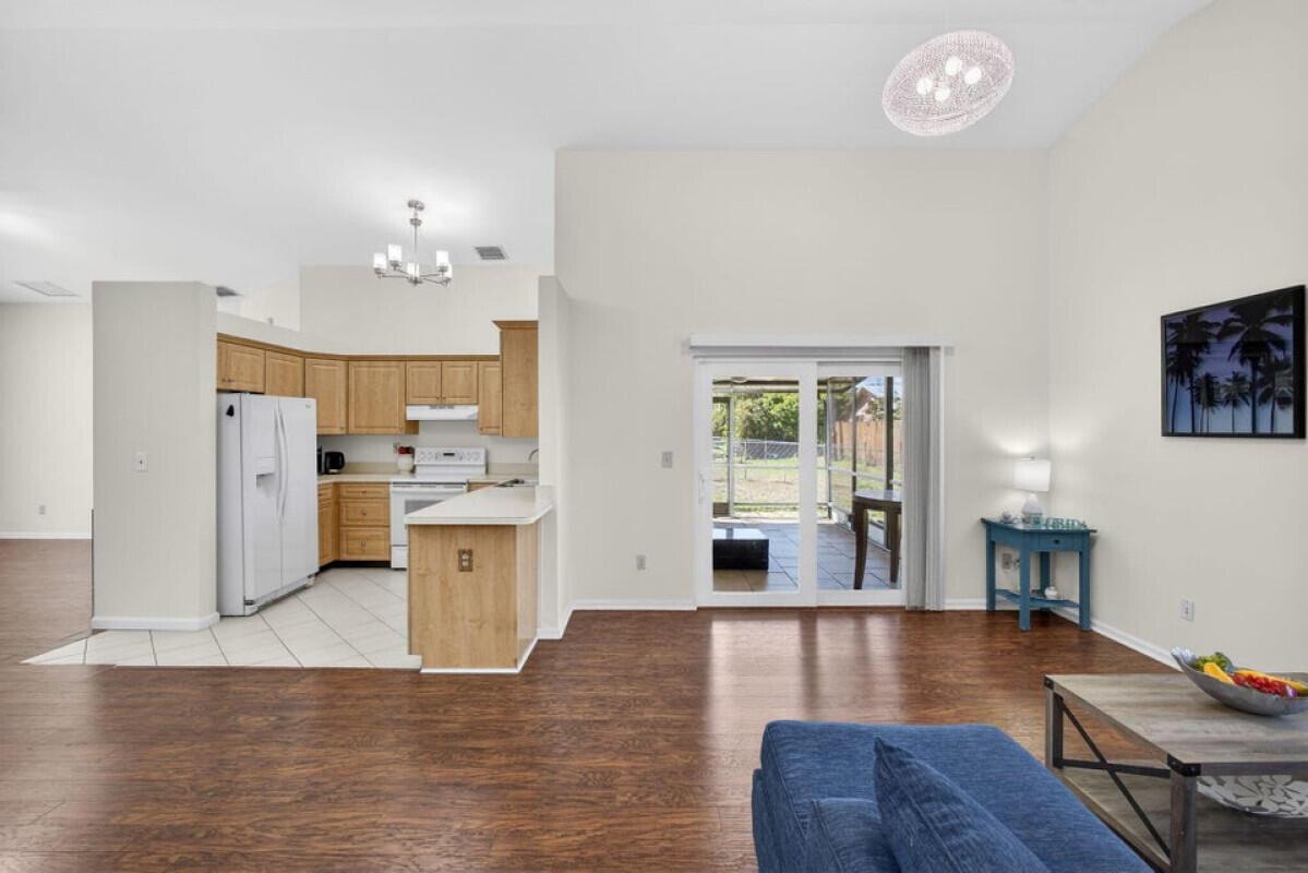 A living room with wood-look flooring opens to a kitchen with light wood cabinets — 6223 Kendrick Street, Jupiter FL 33458, JUPITER, FL