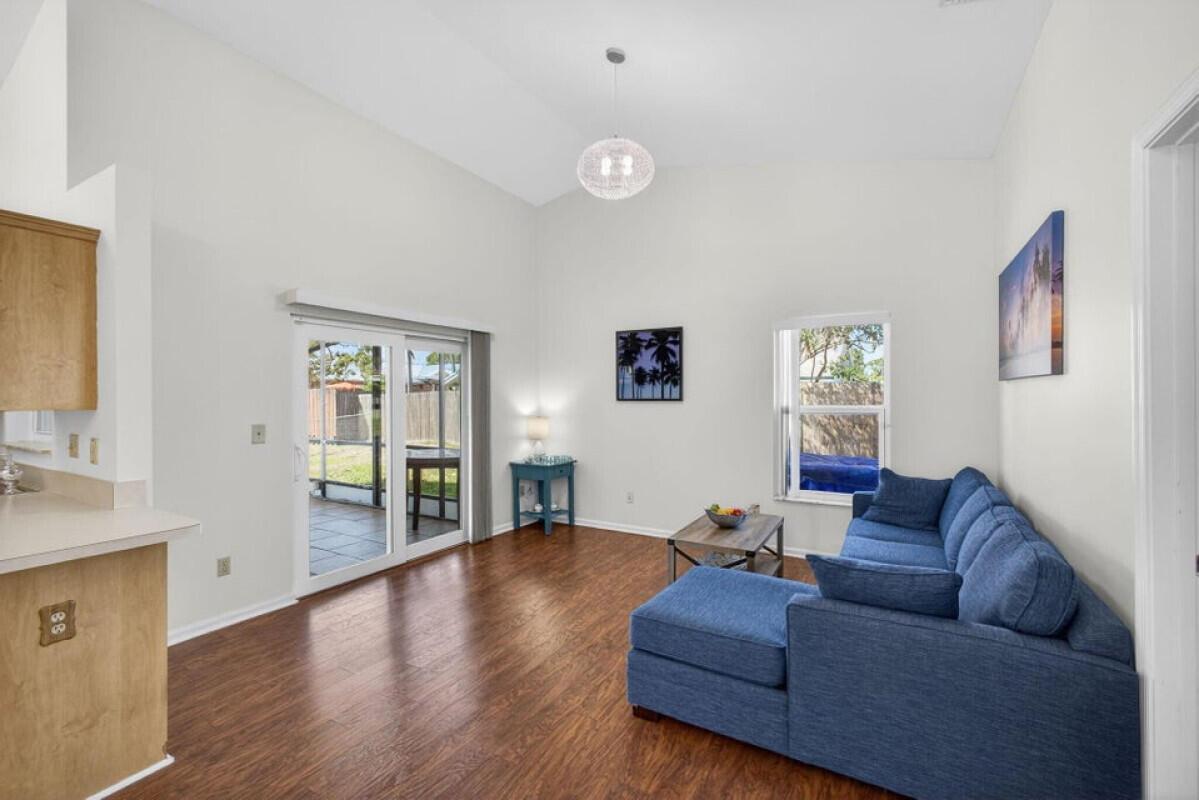 A living room with wood-look flooring, a blue sectional sofa, and a sliding glass door — 6223 Kendrick Street, Jupiter FL 33458, JUPITER, FL