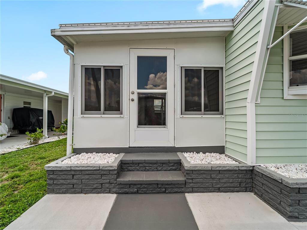 A white enclosed porch entrance features a storm door, sliding windows, and gray brick steps — 3402 SHINGLE OAK TERRACE, SARASOTA, FL