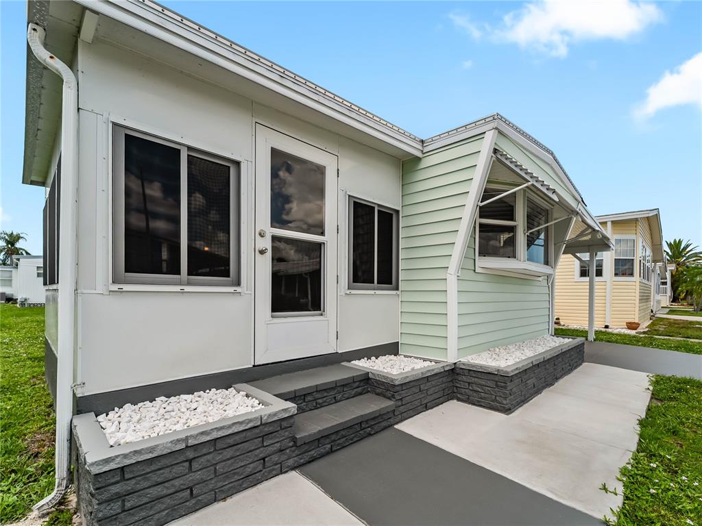 The exterior of a mobile home features light green siding, white trim, and stone planters — 3402 SHINGLE OAK TERRACE, SARASOTA, FL