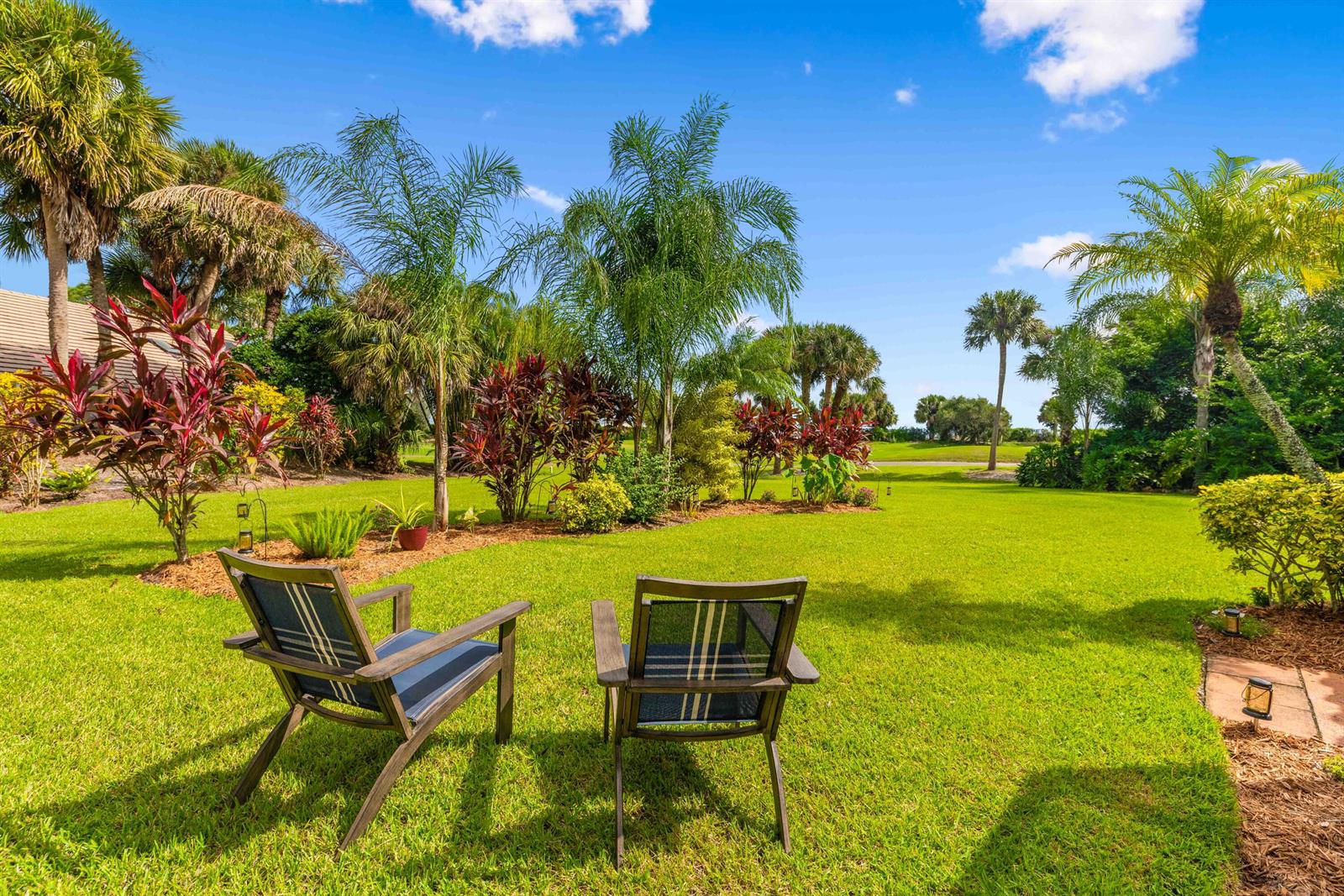 Two outdoor chairs sit on a grassy lawn surrounded by palm trees and tropical landscaping — PORT ST. LUCIE, FL