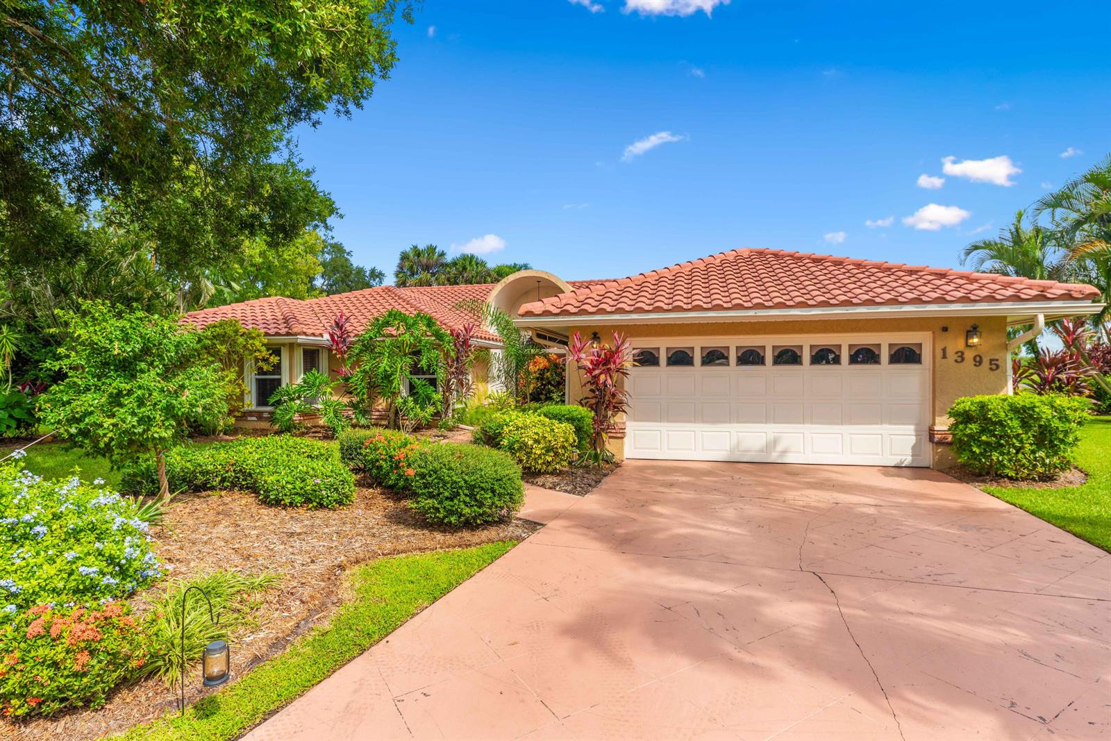 A single-story house with a red tile roof, white garage door, and lush front landscaping — PORT ST. LUCIE, FL