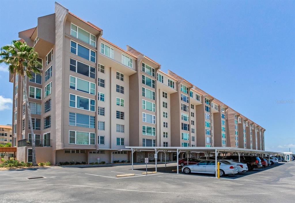 A multi-story apartment building with a covered parking area in front under a clear sky — 632 EDGEWATER DRIVE UNIT 736, DUNEDIN, FL