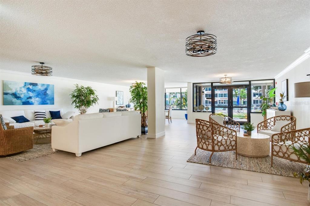 A spacious living room features light wood-look tile floors, white sofas, and wicker accent chairs — 632 EDGEWATER DRIVE UNIT 736, DUNEDIN, FL