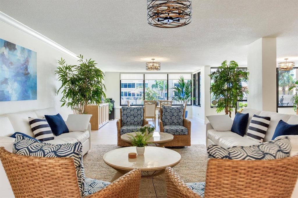 A living room features white sofas, wicker armchairs, patterned cushions, and two large potted plants — 632 EDGEWATER DRIVE UNIT 736, DUNEDIN, FL