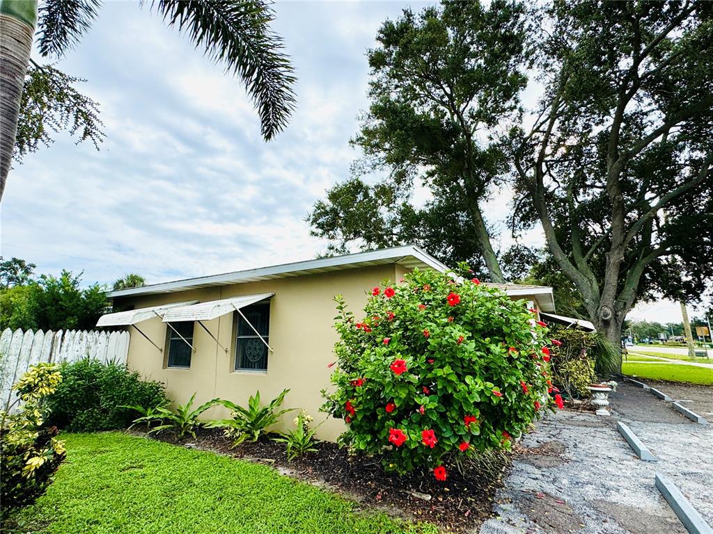 A tan exterior building features white window awnings, a red hibiscus bush, and green landscaping — 5617 GULFPORT BOULEVARD S, GULFPORT, FL