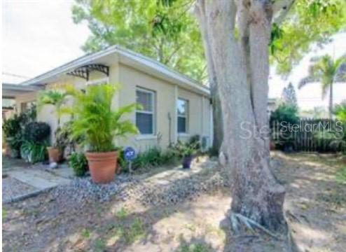 The exterior of a light-colored house features a large tree, potted plants, and gravel landscaping — 5617 GULFPORT BOULEVARD S, GULFPORT, FL