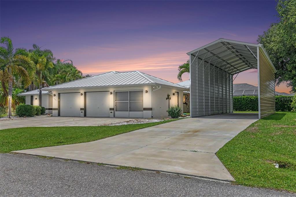 A house exterior with a two-car garage and a detached metal carport on a lawn — 23531 DUNSTAN AVENUE, PORT CHARLOTTE, FL