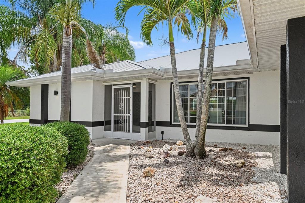 A white house exterior features a screened front entryway, palm trees, and a gravel yard — 23531 DUNSTAN AVENUE, PORT CHARLOTTE, FL