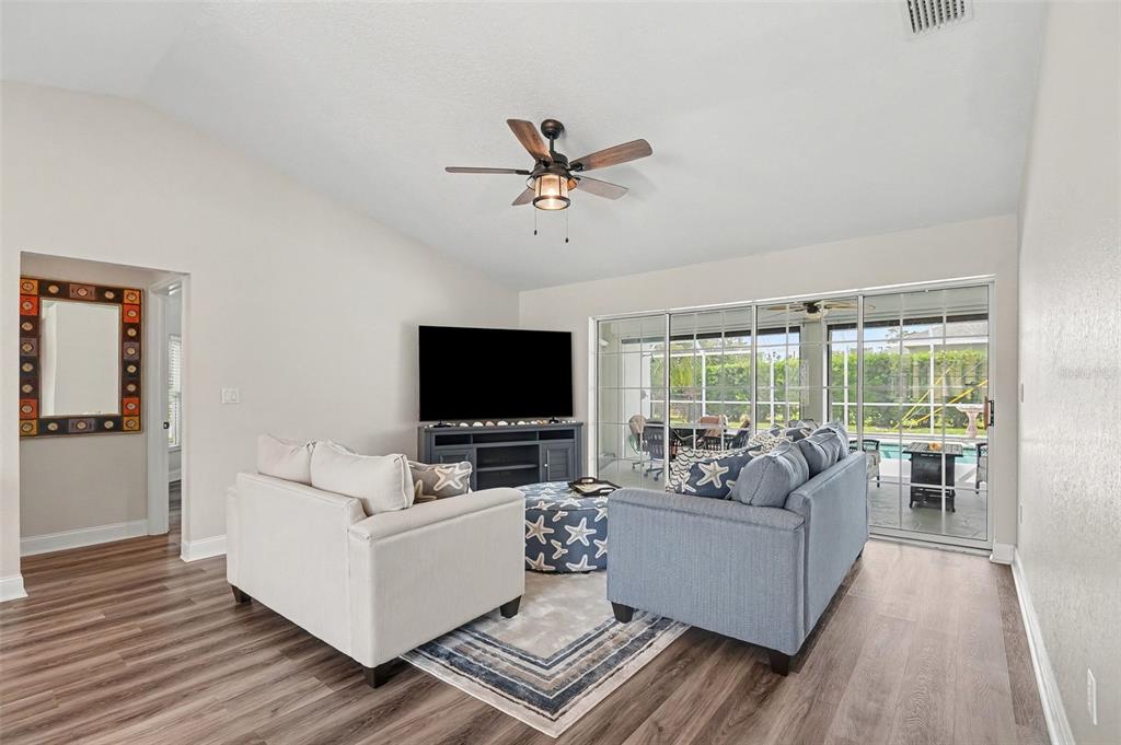 A living room features a blue sofa, white armchair, television, and sliding glass patio doors — 23531 DUNSTAN AVENUE, PORT CHARLOTTE, FL