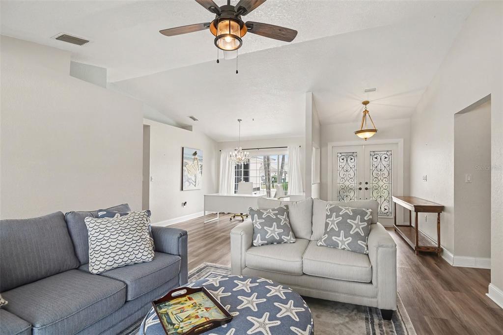 A living room features a blue sofa, a light-colored loveseat, and a matching patterned ottoman — 23531 DUNSTAN AVENUE, PORT CHARLOTTE, FL