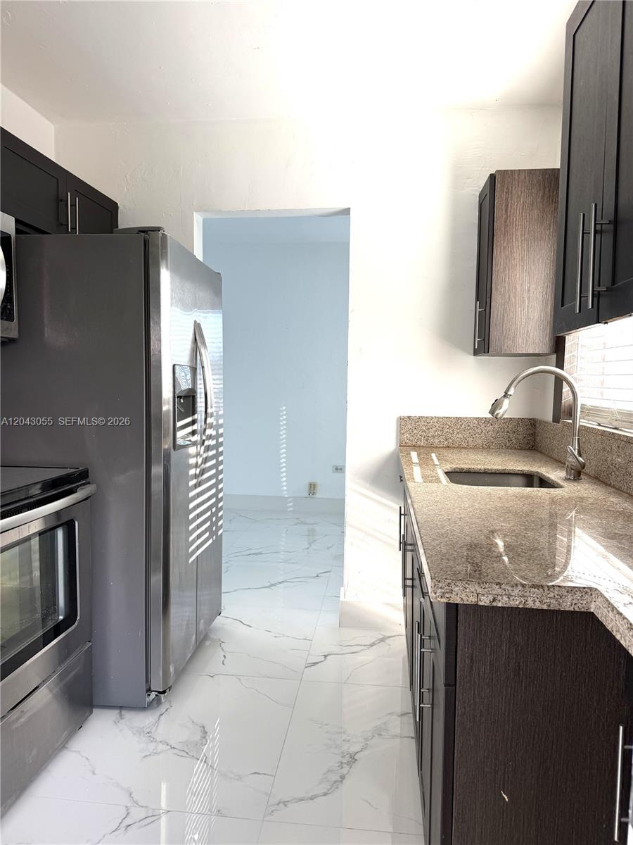 A kitchen features dark wood cabinets, granite countertops, stainless steel appliances, and white marble flooring — 1738 Marseille Dr # 4, Miami Beach FL 33141, MIAMI BEACH, FL
