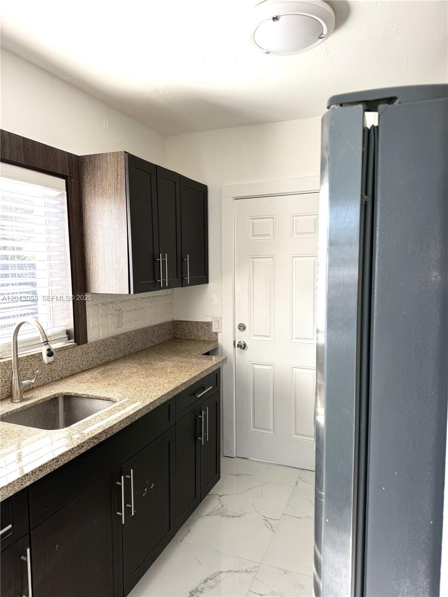 A kitchen features dark cabinets, granite countertops, a stainless steel sink, and white tile flooring — 1738 Marseille Dr # 4, Miami Beach FL 33141, MIAMI BEACH, FL