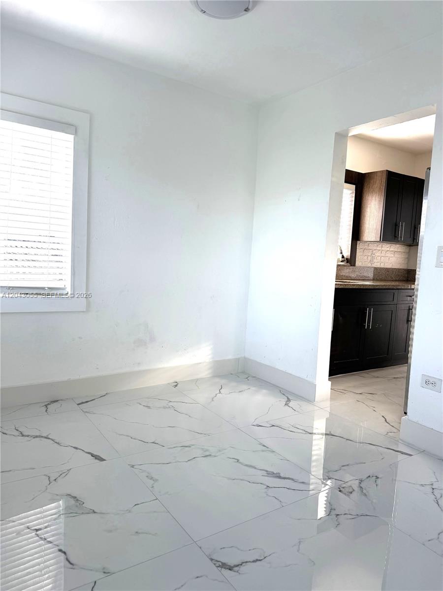 A room with white marble-patterned tile flooring leads into a kitchen with dark cabinets — 1738 Marseille Dr # 4, Miami Beach FL 33141, MIAMI BEACH, FL