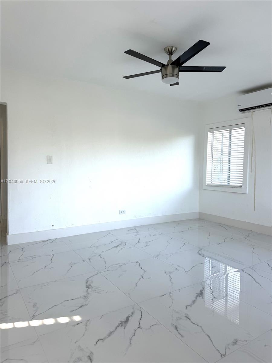 An empty room features white marble-patterned tile flooring, a ceiling fan, and a window — 1738 Marseille Dr # 4, Miami Beach FL 33141, MIAMI BEACH, FL