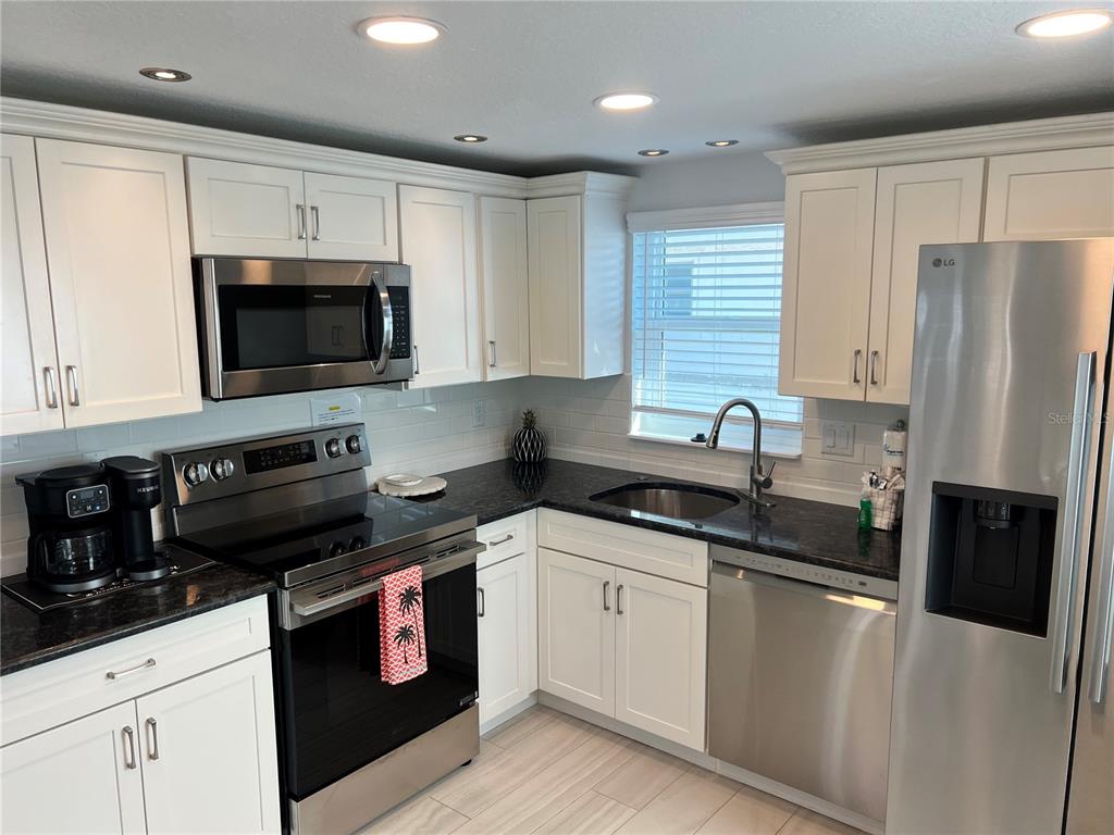 A kitchen features white cabinets, stainless steel appliances, dark countertops, and a subway tile backsplash — 6154 MIDNIGHT PASS ROAD UNIT B02, SARASOTA, FL