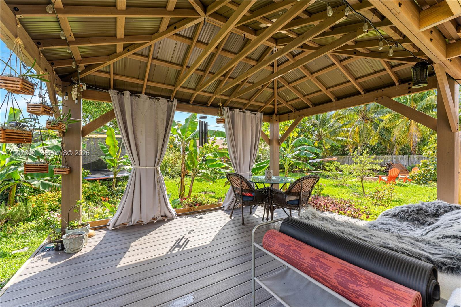A covered wooden deck features a dining set, hanging planters, and views of a garden — 1601 N 16th Ct, Hollywood FL 33020, HOLLYWOOD, FL
