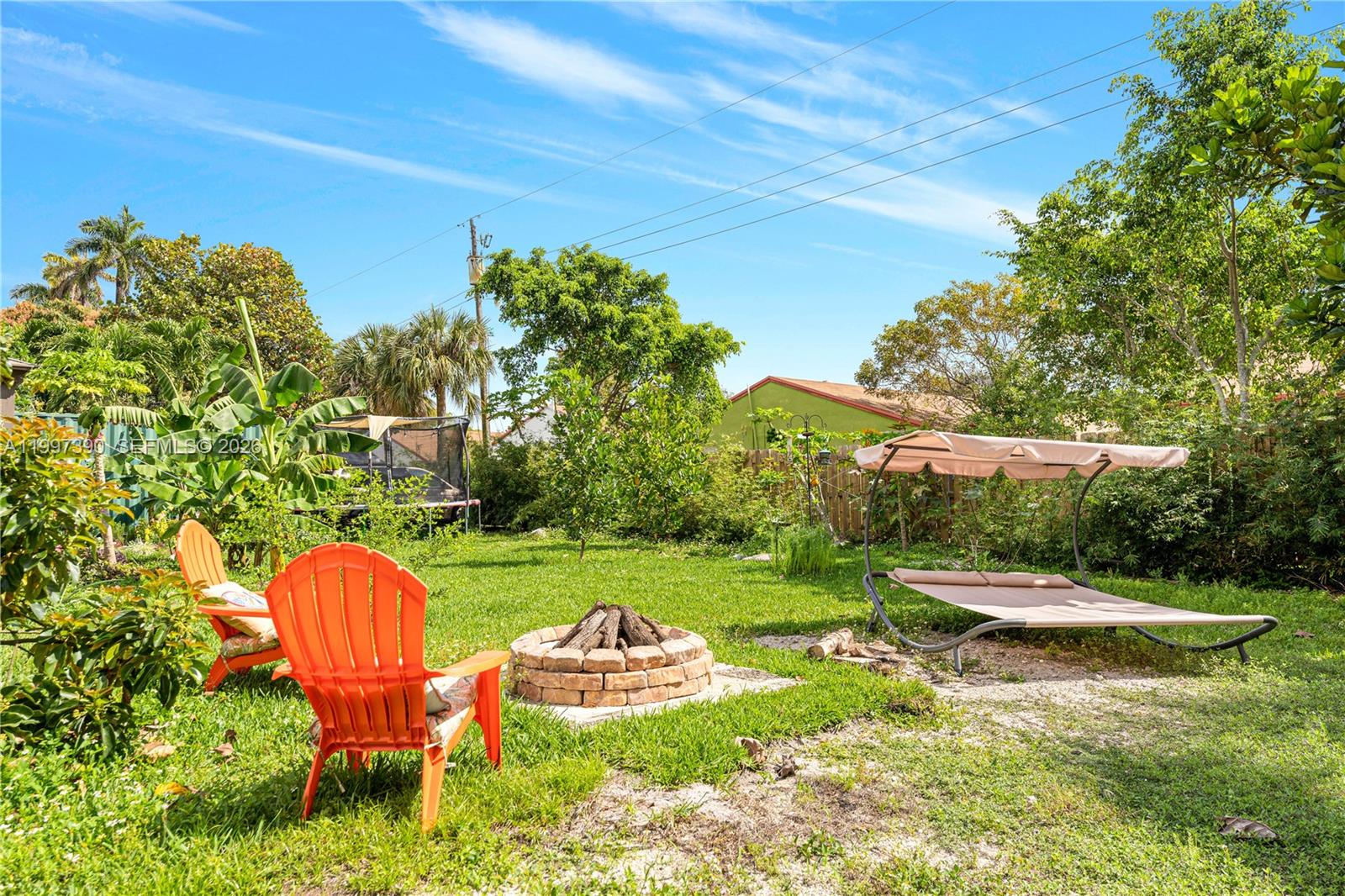A backyard features a brick fire pit, two orange chairs, and a shaded lounge bed — 1601 N 16th Ct, Hollywood FL 33020, HOLLYWOOD, FL