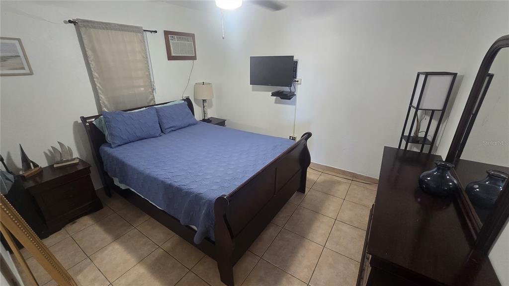 A bedroom features a dark wood sleigh bed, tile flooring, and a wall-mounted television — 3 WILLIAM FONT STREET, CULEBRA, PR